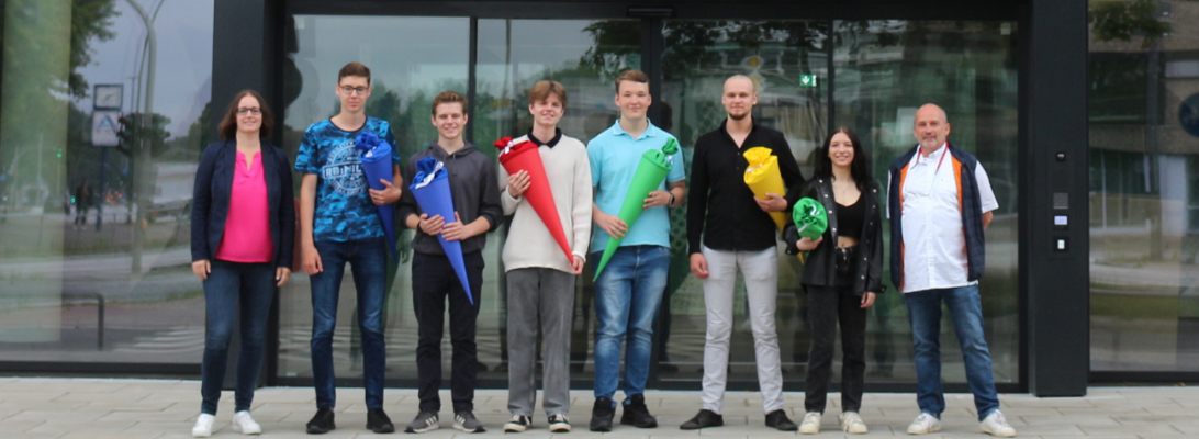 Unser sechs neuen Kolleg*innen für die Ausbildung als Fachinformatiker*in für Systemintegration stehen mit Personalreferentin Sonja und Ausbildungsleiter Andreas vor der Tür.