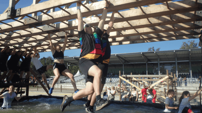 Ricardo und Daniel von der akquinet ONE Solutions hangeln sich an den Monkey Bars durch das erste Hindernis bei den Mud Masters 2023
